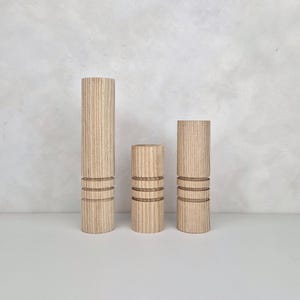 May include: Three wooden dowels with a grooved texture and three horizontal lines carved into each dowel. The dowels are arranged in order of size from left to right.
