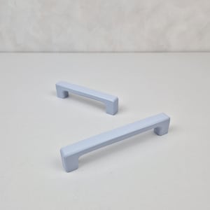 May include: Two light blue cabinet pulls with a rectangular shape. The pulls have a smooth, matte finish.