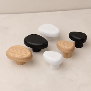Puede incluir: Cinco pomos de armario en forma de guijarro en blanco, negro y madera natural. Los pomos son todos del mismo tamaño y forma, pero tienen diferentes acabados.