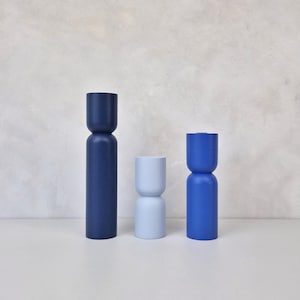 Op de afbeelding: Drie moderne, minimalistische houten sculpturen in blauwtinten. De hoogste is donker marineblauw, de middelste is lichtblauw en de derde is helderblauw. Elk heeft een unieke, geometrische vorm, ideaal voor interieurdecoratie.