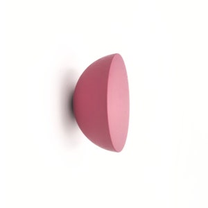 May include: A pink wooden wall hook in the shape of a half sphere.