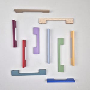 May include: An assortment of colorful cabinet pulls in various shapes and sizes. The pulls are in shades of beige, wood grain, purple, red, light blue, green, yellow, blue, and gray. The hardware is arranged on a white background.