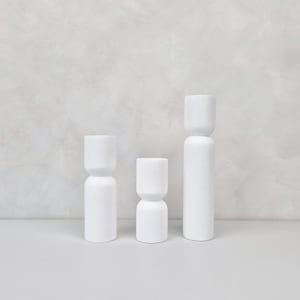 Könnte beinhalten: Drei weiße Kerzenhalter aus Keramik in verschiedenen Höhen. Die Halter sind zylindrisch mit abgerundeter Oberseite und einer leichten Vertiefung in der Mitte.