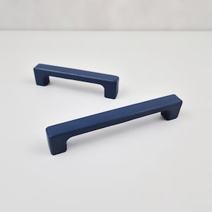 May include: Two blue cabinet pulls with a rectangular shape and rounded edges. The pulls are made of metal and have a matte finish.