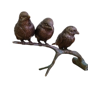 May include: Three bronze bird figurines perched on a branch, with a rustic brown finish. The birds are facing different directions, creating a dynamic composition.