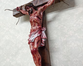 May include: A detailed wooden crucifix featuring a sculpted figure of Jesus Christ. The figure is depicted with visible wounds and a crown of thorns. The cross has a dark wood finish, with text at the top. The figure is tied to the cross with rope.