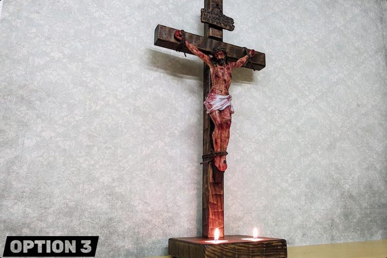 以下が含まれることがあります： イエス・キリストの彫刻が施された木製の十字架。傷と茨の冠が描かれています。十字架は茶色で、人物は白い腰布を着用しています。2本のろうそくが土台に灯っています。「OPTION 3」の文字が下部にあります。