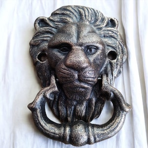 May include: A cast iron lion head door knocker with a distressed bronze finish. The knocker has a detailed face with a mane and a ring for knocking.