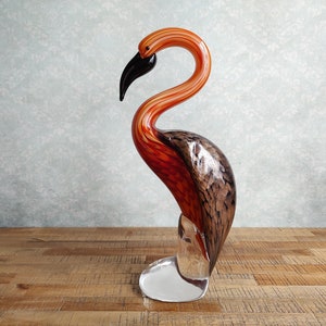 May include: A glass sculpture of a flamingo with orange, red, and black stripes. The flamingo is standing on a clear glass base.