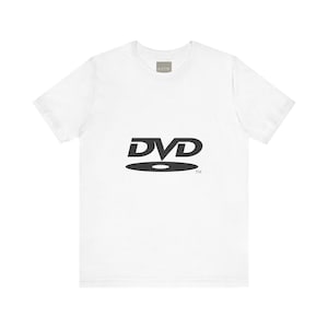 Può includere: T-shirt bianca con logo DVD nero. Il design presenta la parola "DVD" sopra una forma di disco stilizzata. La maglietta ha girocollo e maniche corte, realizzata in materiale morbido.