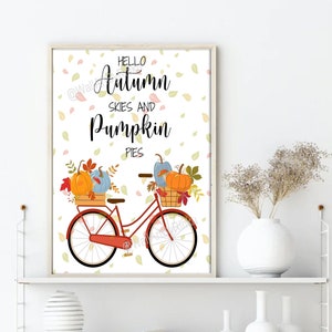 May include: A red bicycle with a basket full of pumpkins and fall leaves. The bicycle is on a white background with a scattered pattern of fall leaves. The text "Hello Autumn Skies and Pumpkin Pies" is written in black on the white background.
