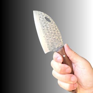 May include: A cleaver-style knife with a textured, silver-colored blade and a wooden handle. The blade has a hole near the top. The knife is held in a hand against a gradient background.