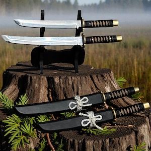May include: Two katana swords with black handles and silver blades are displayed on a black stand. Two additional swords in black sheaths are tied with white rope. The swords are on a tree stump.