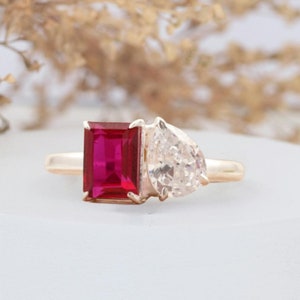 May include: A gold ring with a red emerald-cut gemstone and a pear-shaped diamond.
