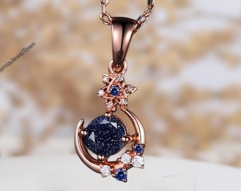 May include: A rose gold necklace with a crescent moon pendant featuring a blue gemstone and smaller blue and white gemstones. The pendant is surrounded by a delicate star design.