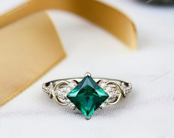 May include: A square emerald engagement ring with a delicate, twisted band and small diamonds on the sides. The ring is set in white gold.