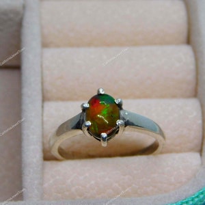 Puede incluir: Un anillo de plata con una piedra preciosa de ópalo verde, rojo y naranja engastada en garras.