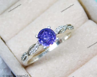 May include: A silver ring with a twisted band and a purple gemstone in the center. The ring is set with small clear stones around the gemstone.
