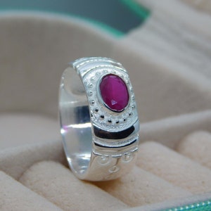 May include: A silver ring with an oval-shaped ruby gemstone set in a decorative band.