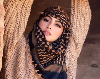 May include: A woman wearing a brown knitted sweater and a black and brown patterned headscarf with tassels. The headscarf is called a keffiyeh.