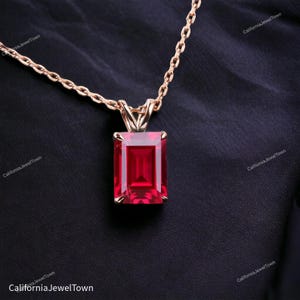 May include: A rose gold chain necklace with a pendant featuring a large, emerald-cut, red gemstone.