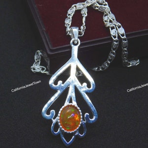 May include: Silver pendant necklace with an oval opal gemstone. The pendant has a decorative, openwork design. The opal displays a mix of orange, red, and green colors. The necklace is displayed on a dark surface.