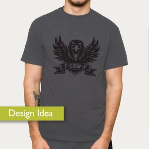 May include: Dark gray t-shirt featuring a black eagle design with outstretched wings and the text "F-CAW-F" on a banner. The eagle graphic is centered on the shirt. The shirt is a short-sleeved crew neck.