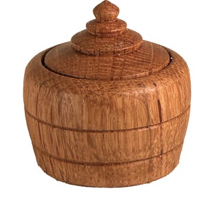 May include: A small wooden box with a lid shaped like a dome. The box is made of light brown wood and has a natural wood finish.