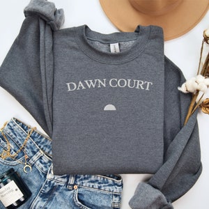 May include: A dark grey sweatshirt with the text "DAWN COURT" in white lettering and a small white crescent moon graphic.