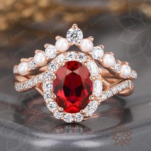 May include: Rose gold ring set featuring a large oval-cut ruby center stone surrounded by a halo of white diamonds. The set includes a matching band with a row of diamonds and a crown-shaped band with pearls and diamonds.