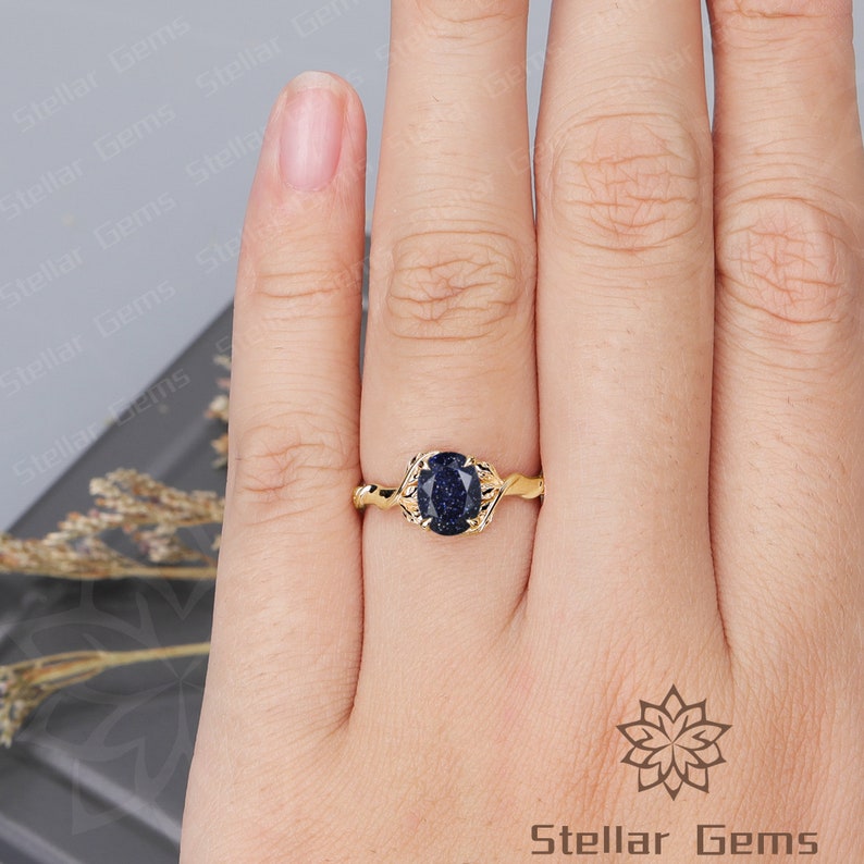 May include: A gold ring with a blue gemstone. The gemstone is oval shaped and has a speckled texture. The ring band is twisted and has a delicate design.