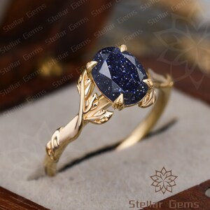 May include: A gold ring with a blue gemstone set in a leaf design. The ring is in a box with the words "Stellar Gems" on the bottom.