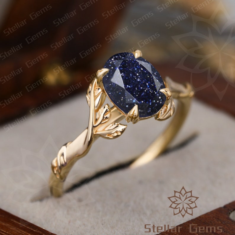May include: A gold ring with a blue gemstone set in a leaf design. The ring is in a box with the words "Stellar Gems" on the bottom.
