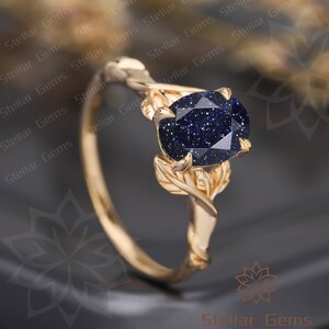 May include: A gold ring with a blue gemstone set in a leaf design. The gemstone is a round, sparkly blue stone with a textured surface.