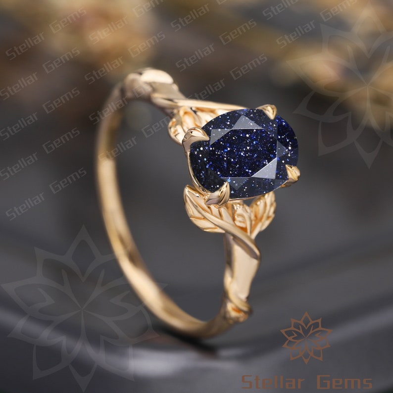 May include: A gold ring with a blue gemstone set in a leaf design. The gemstone is a round, sparkly blue stone with a textured surface.