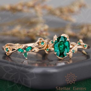 Puede incluir: Un anillo de oro rosa con una piedra central de esmeralda de talla ovalada y pequeños acentos de esmeralda. El anillo presenta un diseño delicado en forma de hoja. El texto "Stellar Gems" es visible en la esquina inferior derecha.