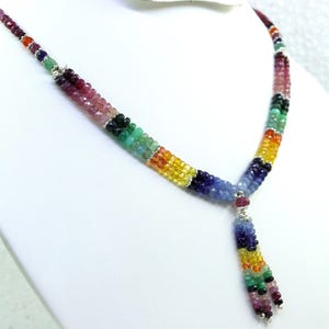 Può includere: Una collana di perline multicolore con un ciondolo a forma di Y. La collana presenta piccole perline rotonde nelle tonalità del rosso, rosa, verde, giallo e blu. Il ciondolo è un nappa di perline simili.