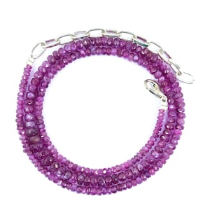 Op de afbeelding: Een ketting met een streng kleine, gefacetteerde, diepmagenta edelsteenkralen in een cirkelvormig patroon. De ketting is voorzien van een zilverkleurige metalen verlengketting met ovale schakels en een karabijnsluiting aan het uiteinde.