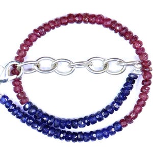 May include: A two-strand necklace featuring alternating rows of deep red and dark blue gemstones. The necklace is connected by a silver-colored chain and clasp. The gemstones are faceted, catching the light.