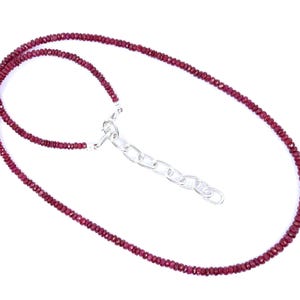 May include: A delicate necklace featuring small, faceted ruby beads in a deep red hue. The necklace is strung together and has a silver-colored chain and clasp. The necklace is displayed against a white background.