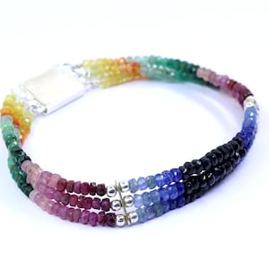 May include: A multi-strand bracelet featuring a spectrum of colors, from vibrant yellows and greens to deep blues and blacks. The bracelet is composed of small, faceted beads and has a silver-toned clasp.