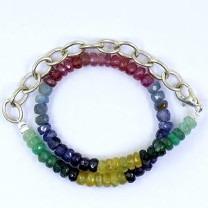 May include: A multi-strand bracelet featuring a chain link design and a spectrum of colorful gemstones. The gemstones include red, blue, green, and yellow hues. The bracelet is secured with a silver clasp.