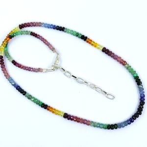 May include: A colorful beaded necklace with a silver chain clasp. The necklace features a gradient of colors, including red, yellow, green, blue, and purple. The beads are small and round, creating a vibrant and eye-catching accessory.
