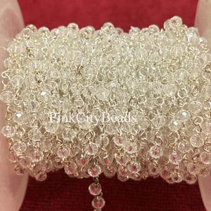 May include: A spool of clear crystal beads strung on silver wire. The beads are faceted, reflecting light, and are tightly wound around a white plastic spool. The text "Pink City Beads" is visible on the spool.