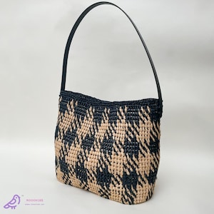 May include: A woven handbag with a black leather strap. The bag features a geometric pattern in black and beige. The bag is rectangular with a curved top and a single strap.