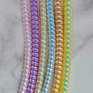 May include: Five vertical, iridescent, coiled plastic cords arranged side-by-side. The colours from left to right are light pink, purple, light yellow, light blue, and orange, with a final yellow cord on the far right, all featuring a shiny finish.