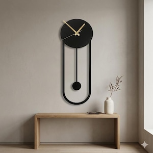May include: A modern black wall clock with gold-colored hands. The clock has a circular face and a long, vertical, U-shaped frame with a circular pendulum. The clock is mounted on a neutral-colored wall.