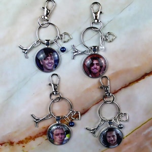 Peut inclure: Quatre porte-clés en métal argenté avec des cabochons en verre circulaires présentant des portraits de différentes personnes. Chaque porte-clé comprend un fermoir mousqueton, un anneau, un petit cœur, une crosse de hockey et une perle colorée.