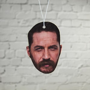 May include: A car air freshener featuring a close-up image of a man's face with a beard and moustache.