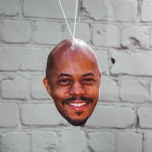 Puede incluir: Un ambientador de coche con una foto de primer plano de la cara de un hombre sonriendo.